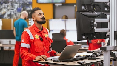 A professional in a red uniform with a badge and lanyard is focused on work at a laptop