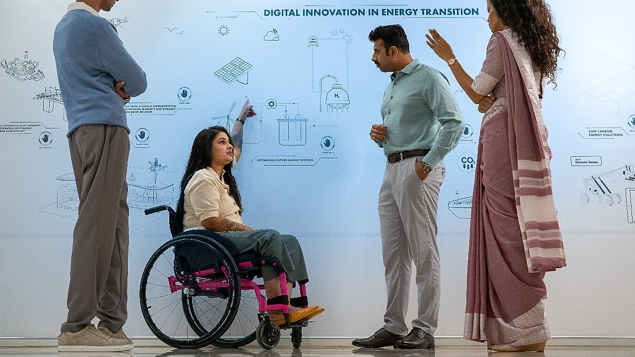 A group of four individuals is standing in front of a large whiteboard with diagrams and text related to “Digital Innovation in Energy Transition.” One person in a wheelchair is pointing at the board, indicating active participation in a  discussion.​