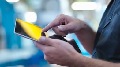 Person operating a touchscreen smartphone in an industrial setting.