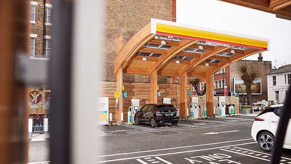 Modern electric vehicle charging station with wooden architecture and multiple charging units, with a car parked for charging.
