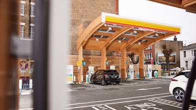Modern electric vehicle charging station with wooden architecture and multiple charging units, with a car parked for charging.
