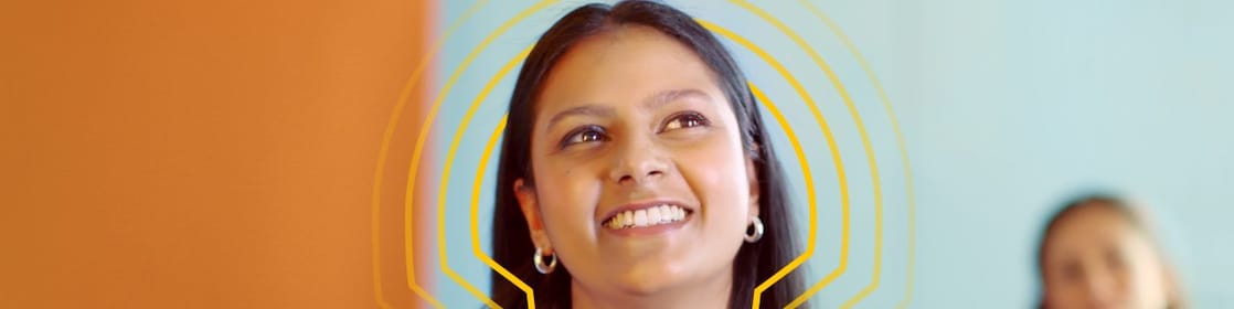 An Indian woman in a blue shirt smiles while looking up, with pecten energy lines overlay. Another person is in the blurred background.
