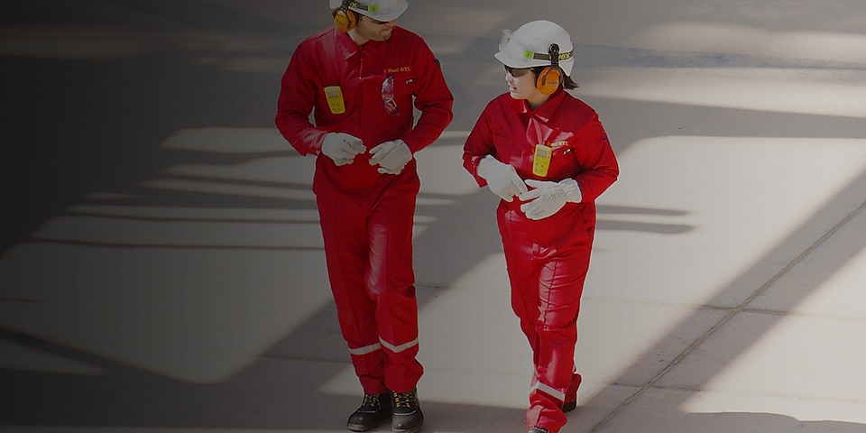 Male and female worker in red overalls and white helmets and hearing protection walking
