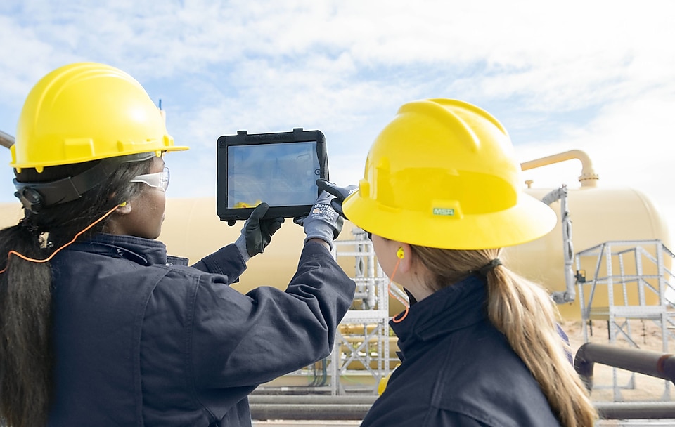 Two women with protective equipment an iPad at an oil plant