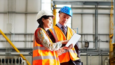 Two warehouse workers talking together over a digital tablet.