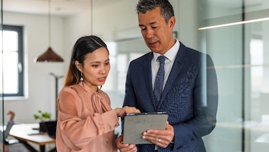 Business discussion between two colleagues working in a meeting room, using a digital tablet.