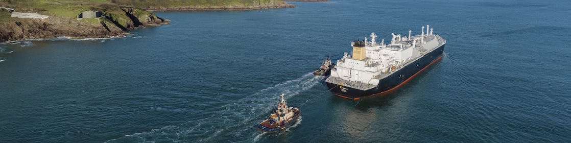 Cargo ship in the middle of water passing land.
