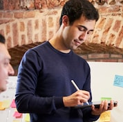 Male drawing on iPad with sticky notes on a whiteboard in the background.