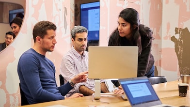 Two males and one female mid conversation around a laptop.