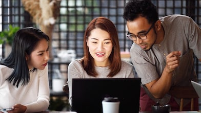 Two females and one male looking at a laptop screen in a coffee shop environment