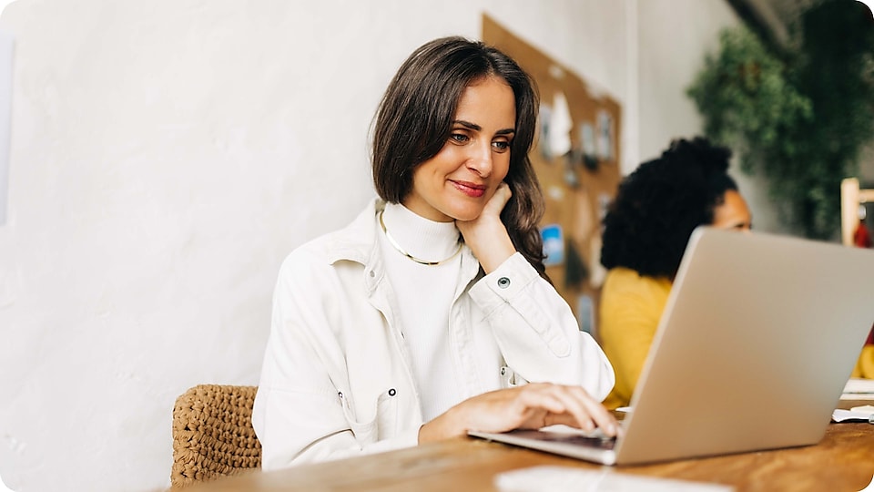 A woman sitting in an office setting working on laptop looking happy